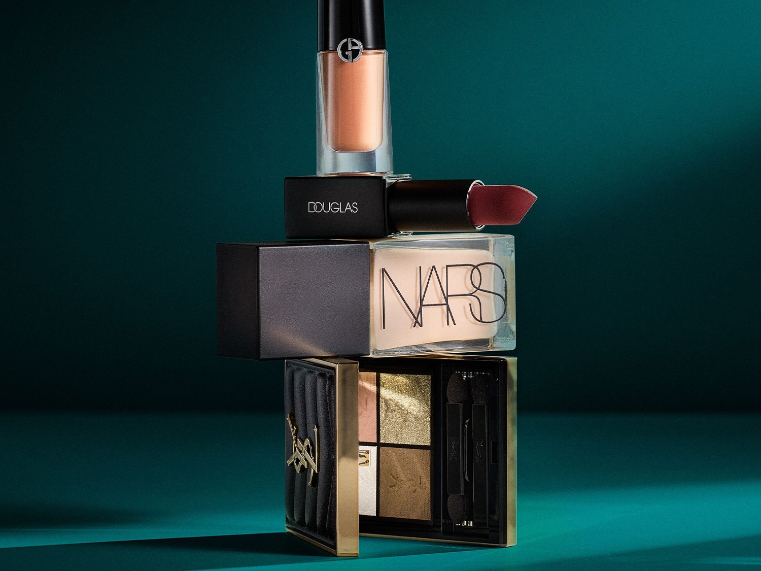 Ein Turm aus Make-up-Produkten, darunter Lidschattenpalette, Lippenstift und Foundation, gestapelt vor einem dunkelgrünen Hintergrund.