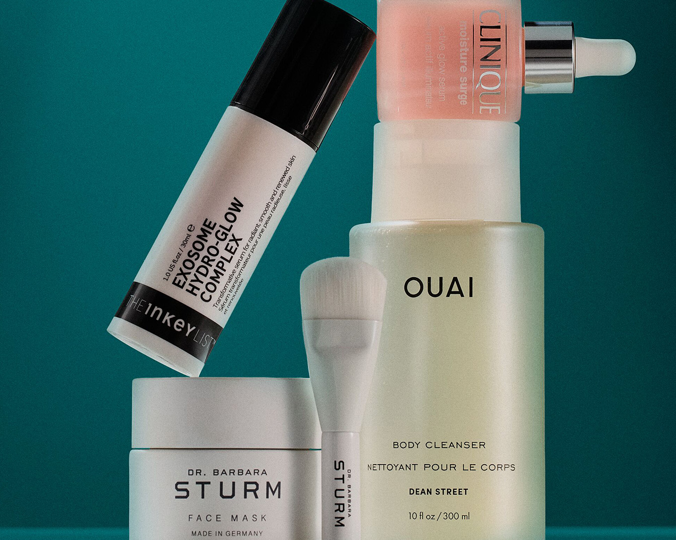 Auf einem türkisfarbenen Hintergrund sind Hautpflegeprodukte von Clinique, Dr. Barbara Sturm und The Inkey List zu sehen, darunter Seren, Gesichtsmasken und ein Pinsel.
