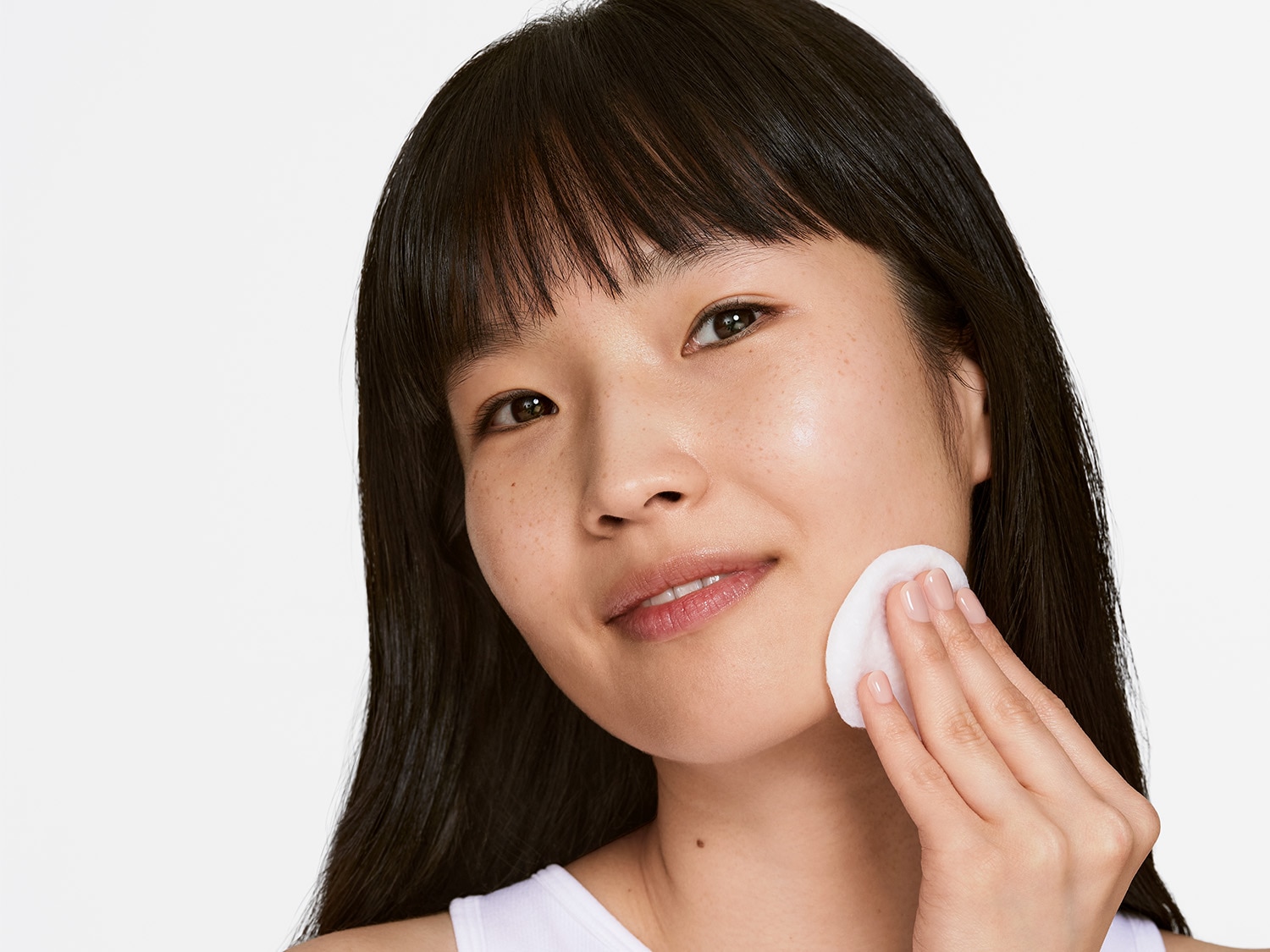 Eine Frau mit dunklen Haaren reinigt ihr Gesicht mit einem Wattepad.