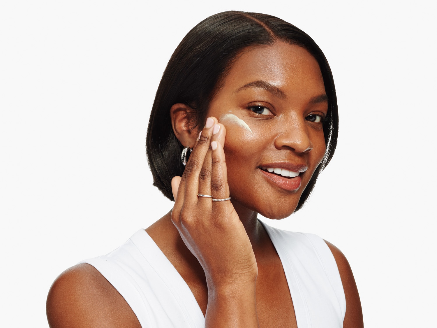 Eine lächelnde Frau trägt eine Feuchtigkeitscreme auf ihre Wange auf.