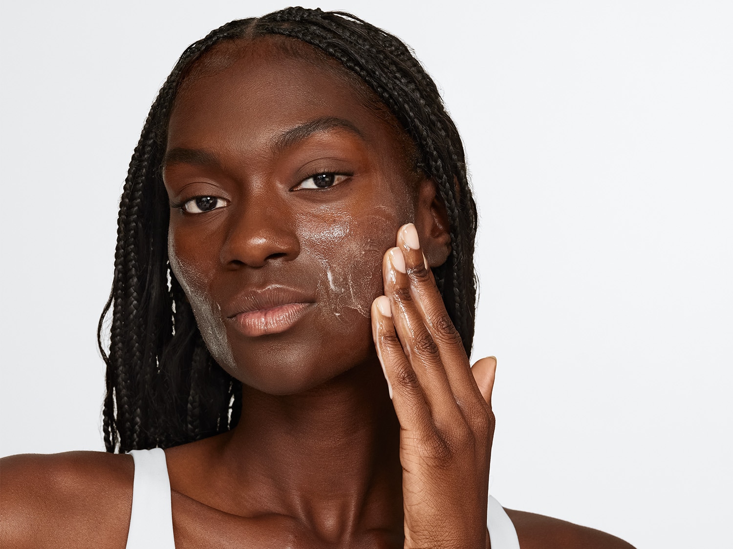 Eine Frau mit geflochtenem Haar massiert eine klare Flüssigkeit auf ihr Gesicht.