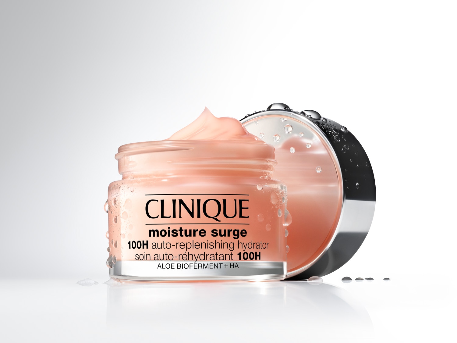 Nahaufnahme eines Tiegels Clinique Moisture Surge 100H Auto-Replenishing Hydrator mit rosa Creme und silbernem Deckel, der mit Wassertropfen bedeckt ist.