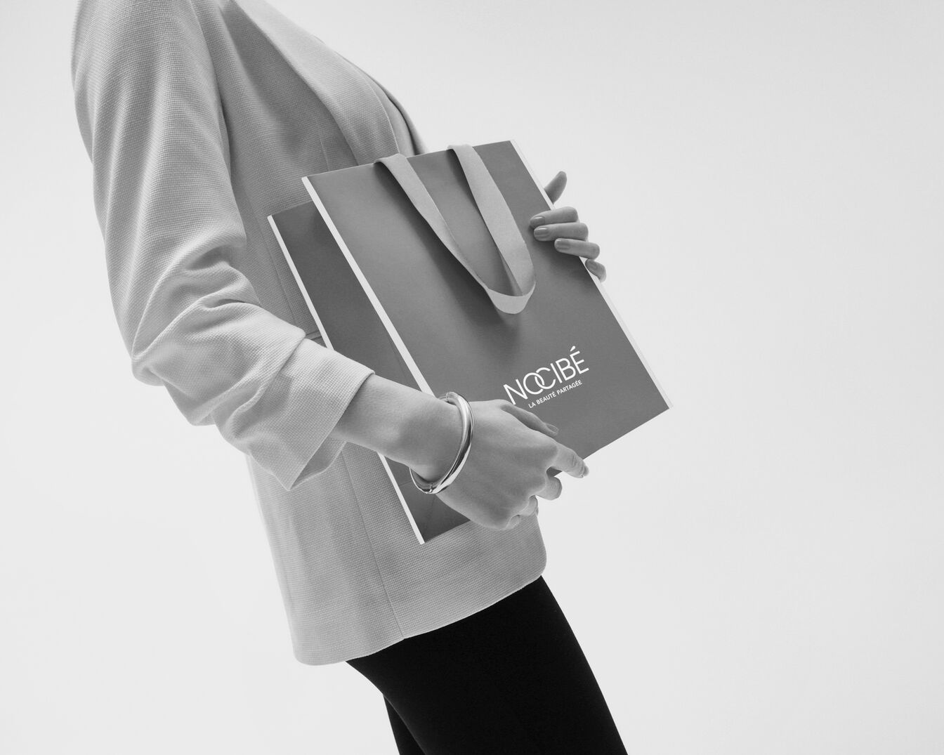 Une femme élégante tient un sac Nocibé, symbole de beauté partagée et de produits de qualité.