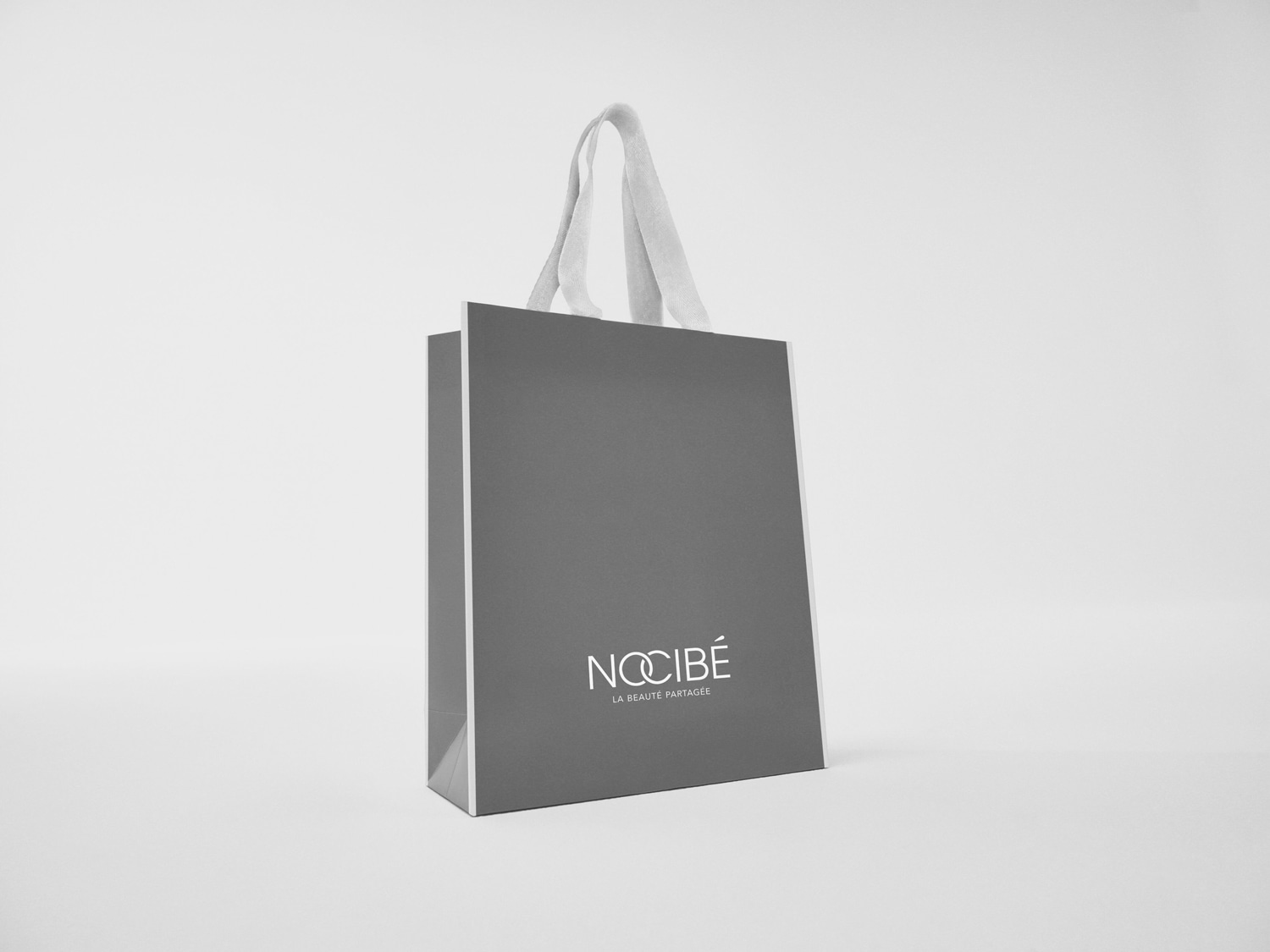 Sac gris Nocibé avec des poignées blanches, portant le slogan 'La beauté partagée'.