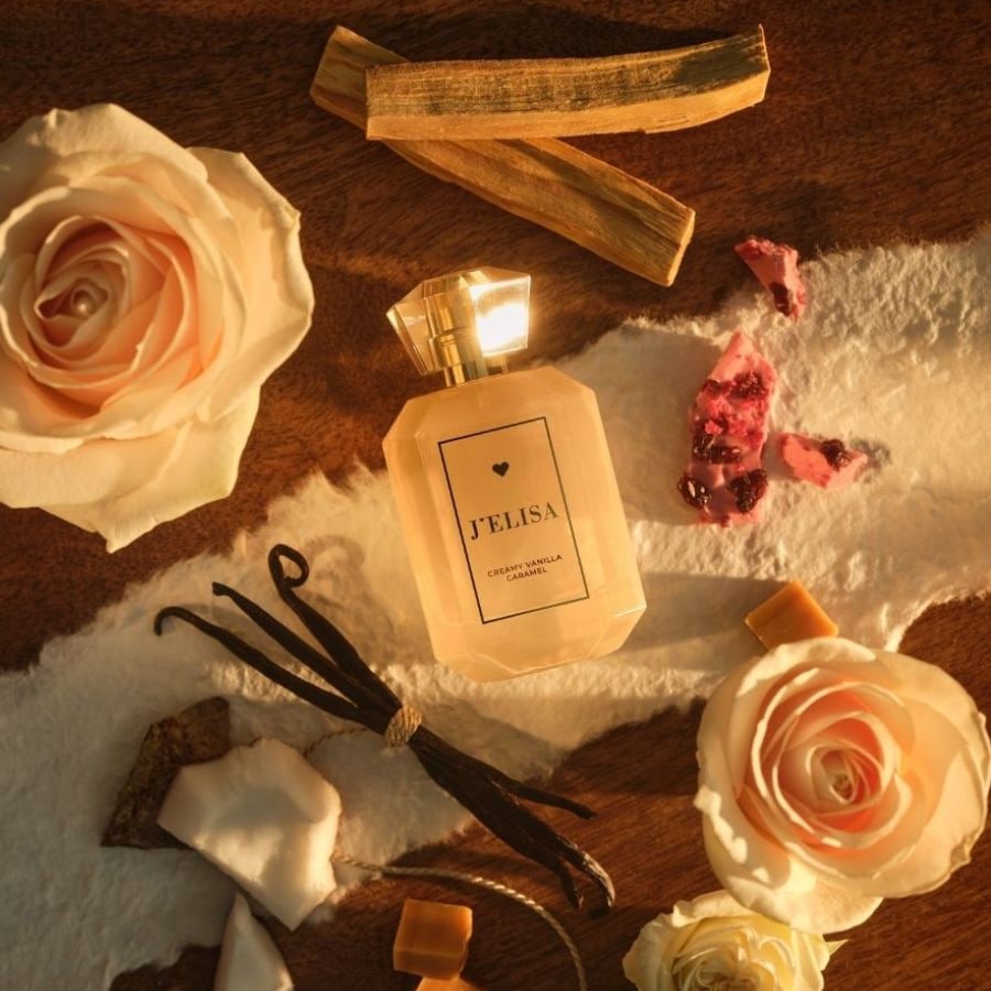 Ein Flakon J'ELISA Creamy Vanilla Caramel Duft steht inmitten von Rosen, Vanilleschoten und Karamellstücken auf einem warmen, hölzernen Untergrund.