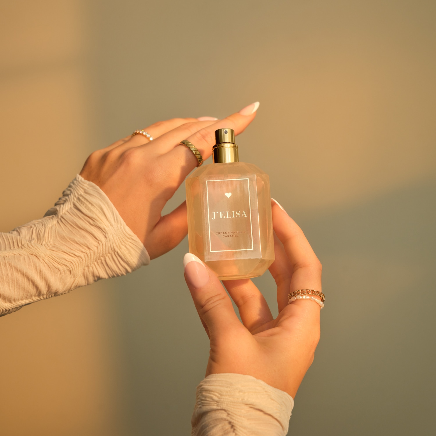 Die Hände halten eine Flasche J'elisa Creamy Vanilla Caramel Parfüm mit goldenem Sprühkopf.
