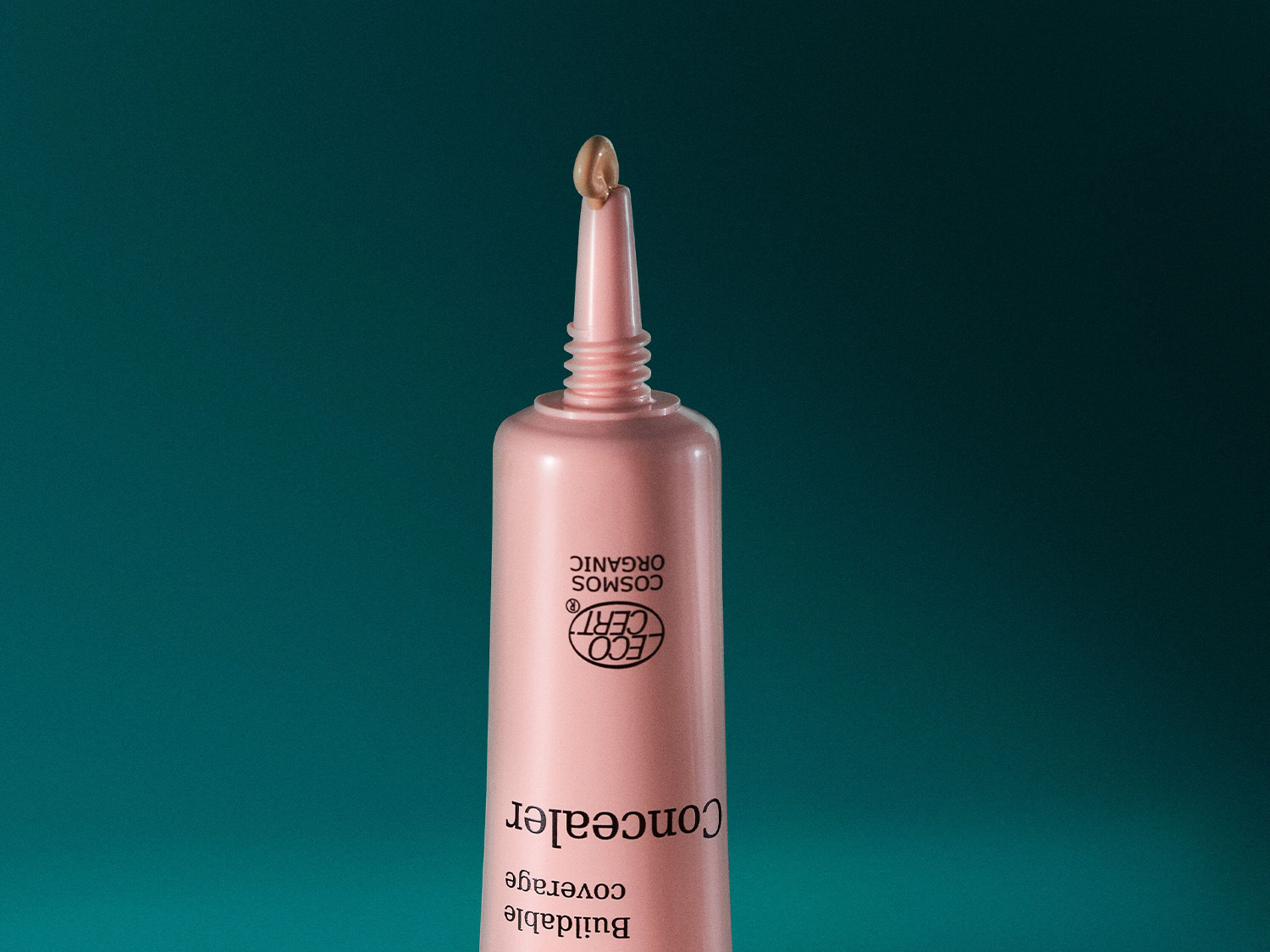 Nahaufnahme einer hellrosa Tube mit Concealer, der mit „ECO CERT COSMOS ORGANIC“ zertifiziert ist und eine cremige Textur für eine aufbaubare Deckkraft bietet.