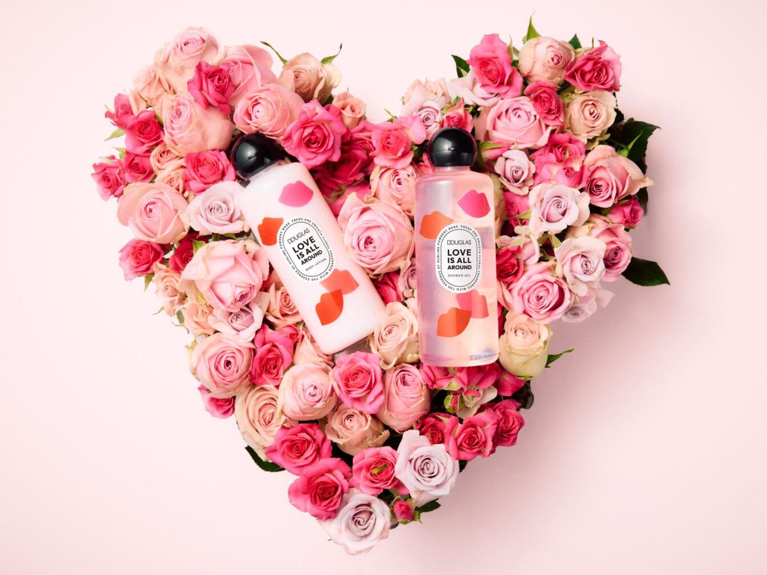Roze rozen vormen een hartvormige achtergrond voor Douglas 'Love is All Around' bodylotion en douchegel, beide met een fris roze rozenparfum.
