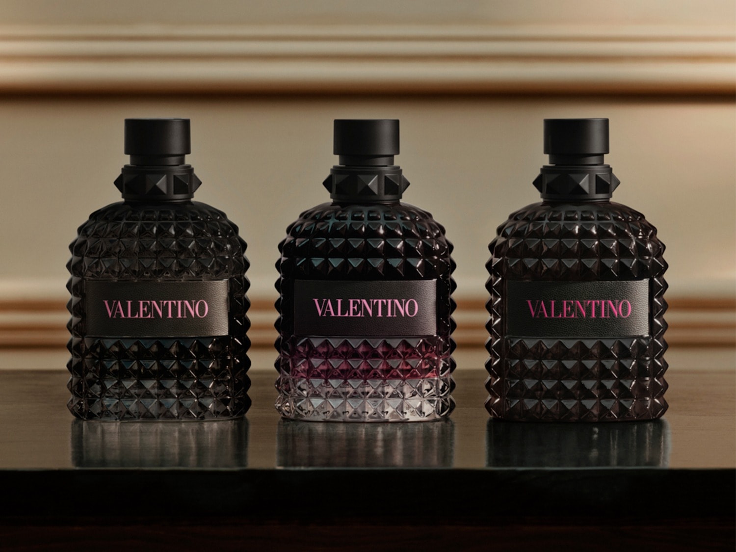 Drie Valentino geuren staan op een donkere tafel, de flessen zijn donker met een roze Valentino label.