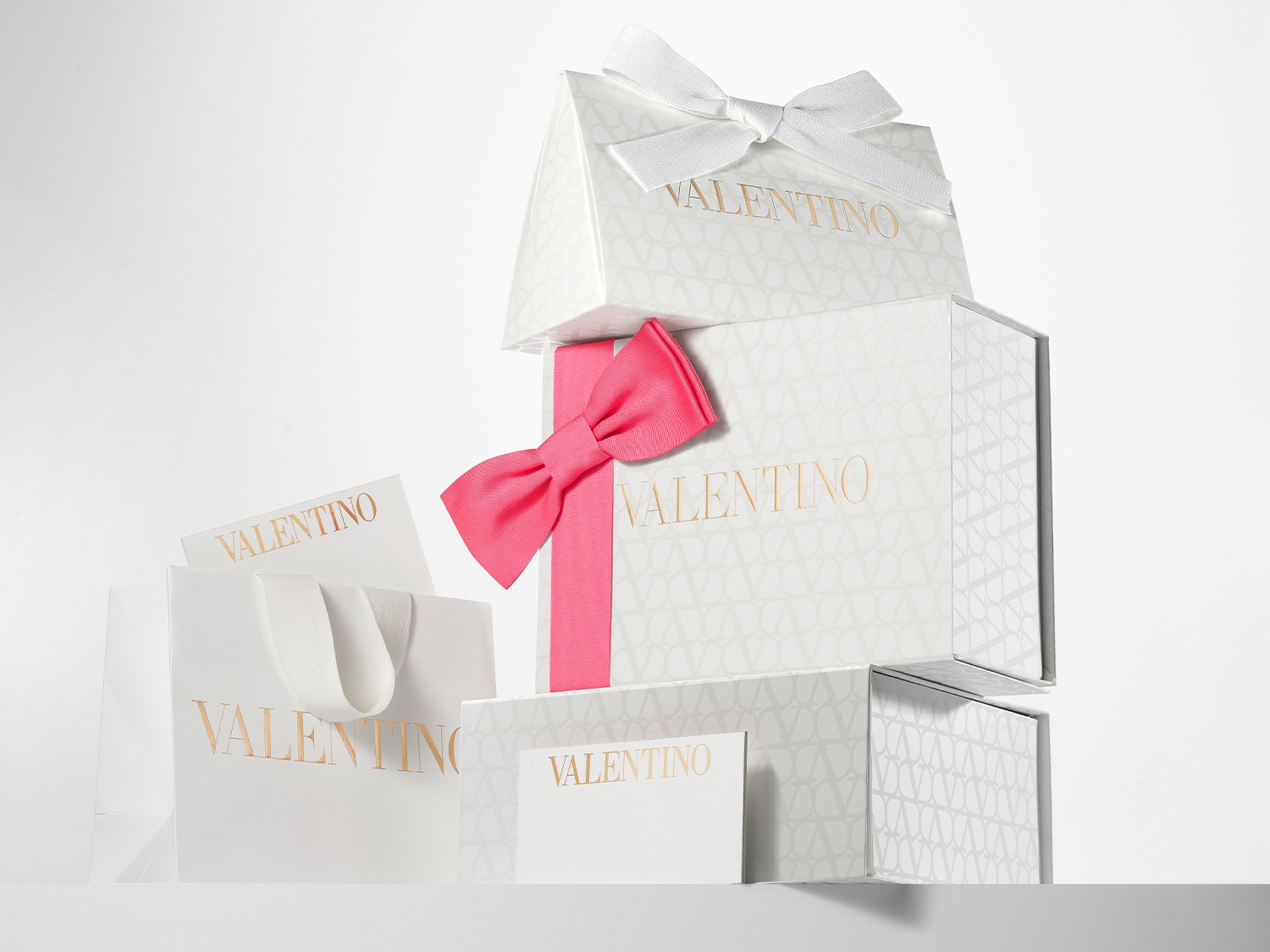 Gestapelde Valentino geschenkdozen en een tas, versierd met een witte en roze strik, klaar om iemand speciaal te verrassen.