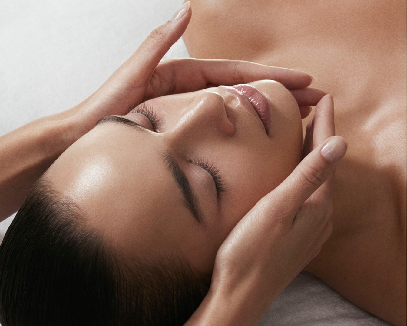 Gros plan sur un visage féminin recevant un massage facial, les mains douces exerçant une pression apaisante pour une peau éclatante et détendue.