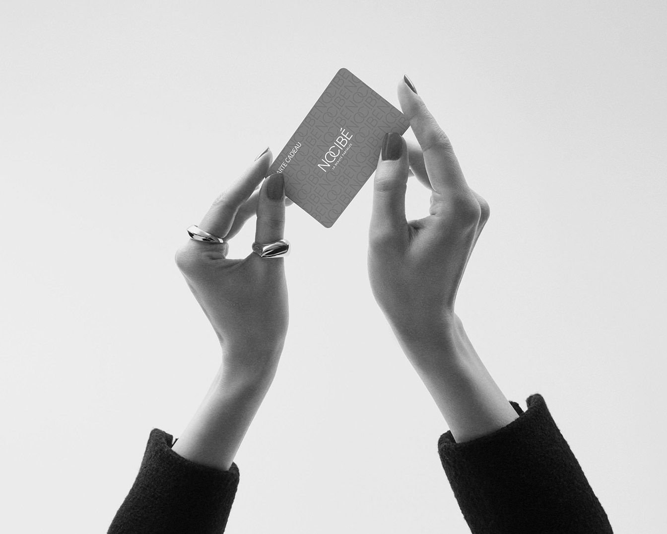 Gros plan sur une carte cadeau Nocibé tenue par deux mains élégantes, parfait pour offrir la beauté.