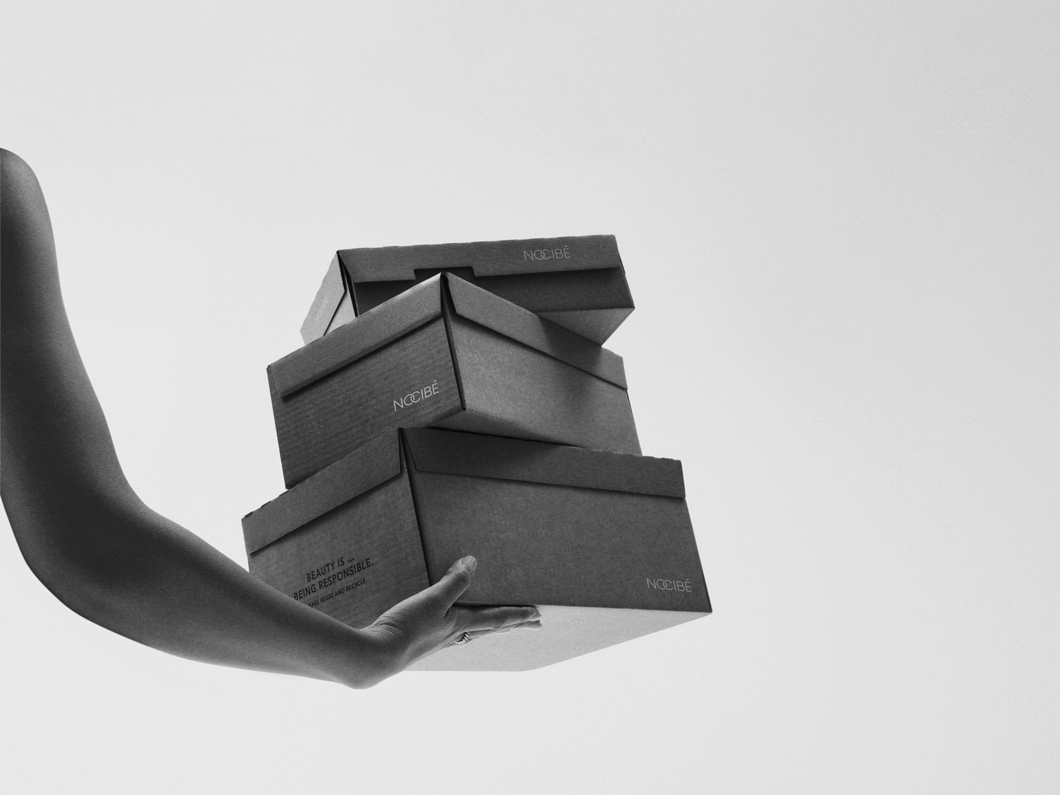Une main tenant une pile de boîtes Nocibé en carton, soulignant l'engagement de la marque envers la responsabilité environnementale : la beauté est synonyme de réutilisation et de recyclage.