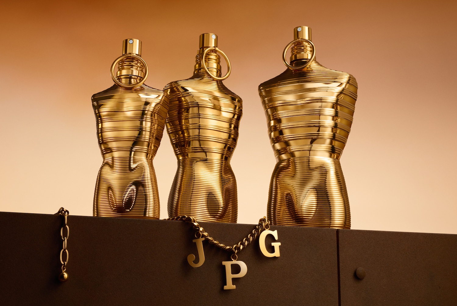 Drei goldene Flakons in Form von Männerkörpern stehen auf einem Sockel, verziert mit einer goldenen Kette mit den Buchstaben JPG.