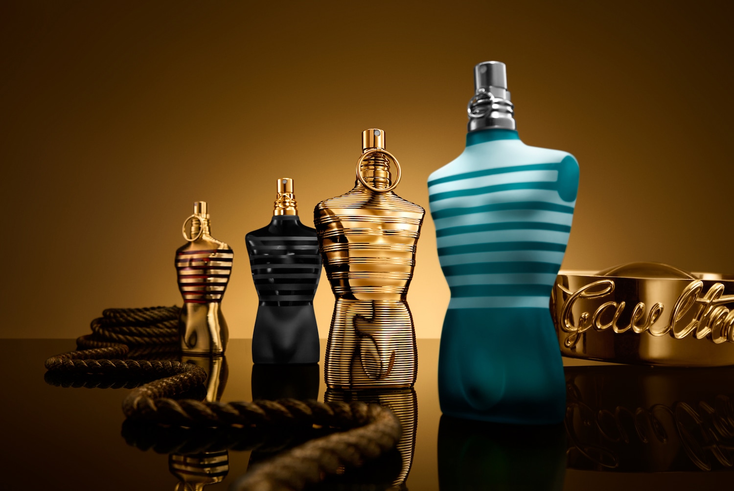 Eine Reihe von Jean Paul Gaultier Parfümflaschen in Form von männlichen Torsos, die in verschiedenen Farben und Ausführungen auf einem glänzenden Untergrund präsentiert werden.