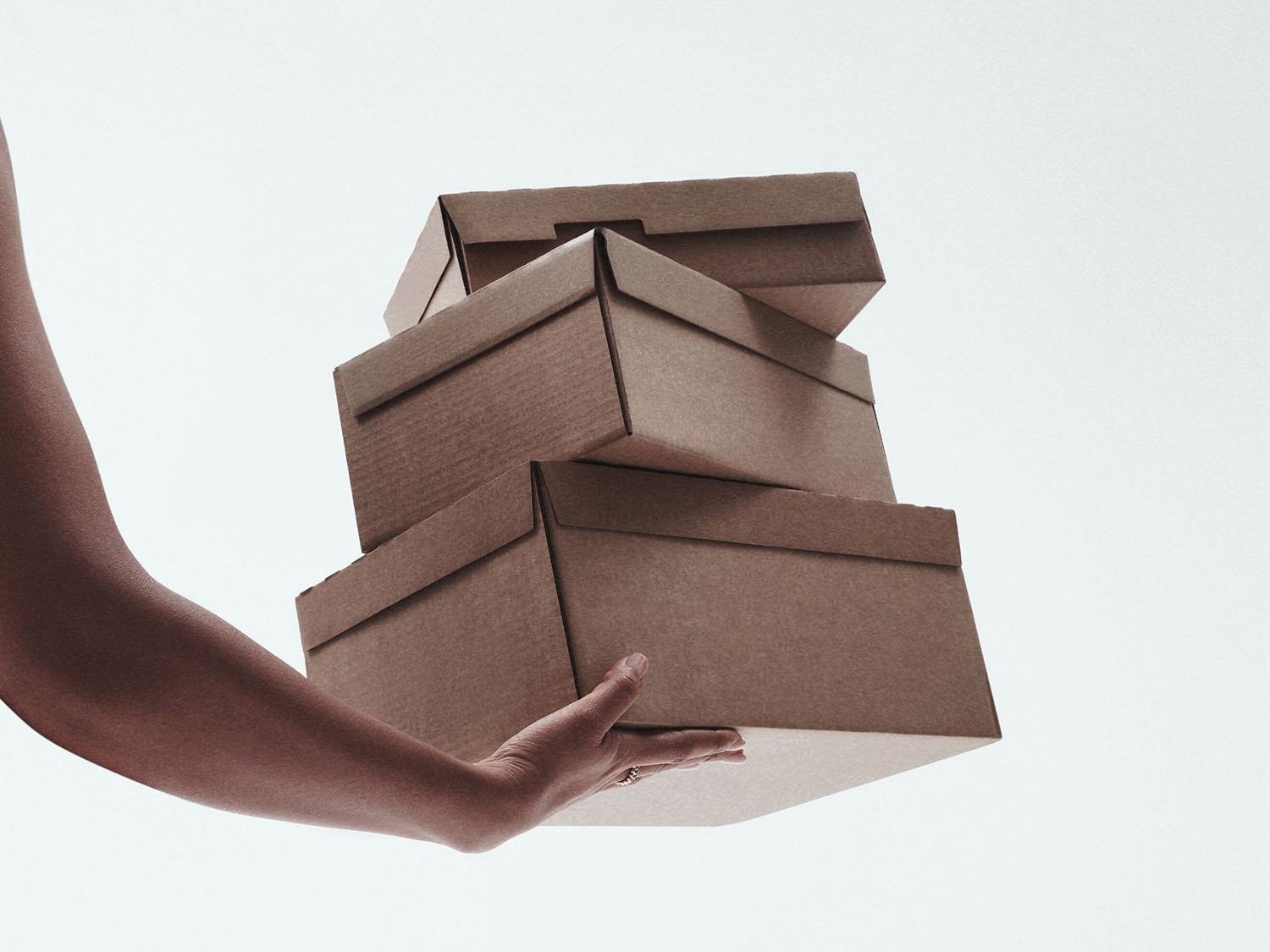 Une main tient une pile de quatre boîtes d'expédition en carton brun, suggérant une livraison ou un envoi.