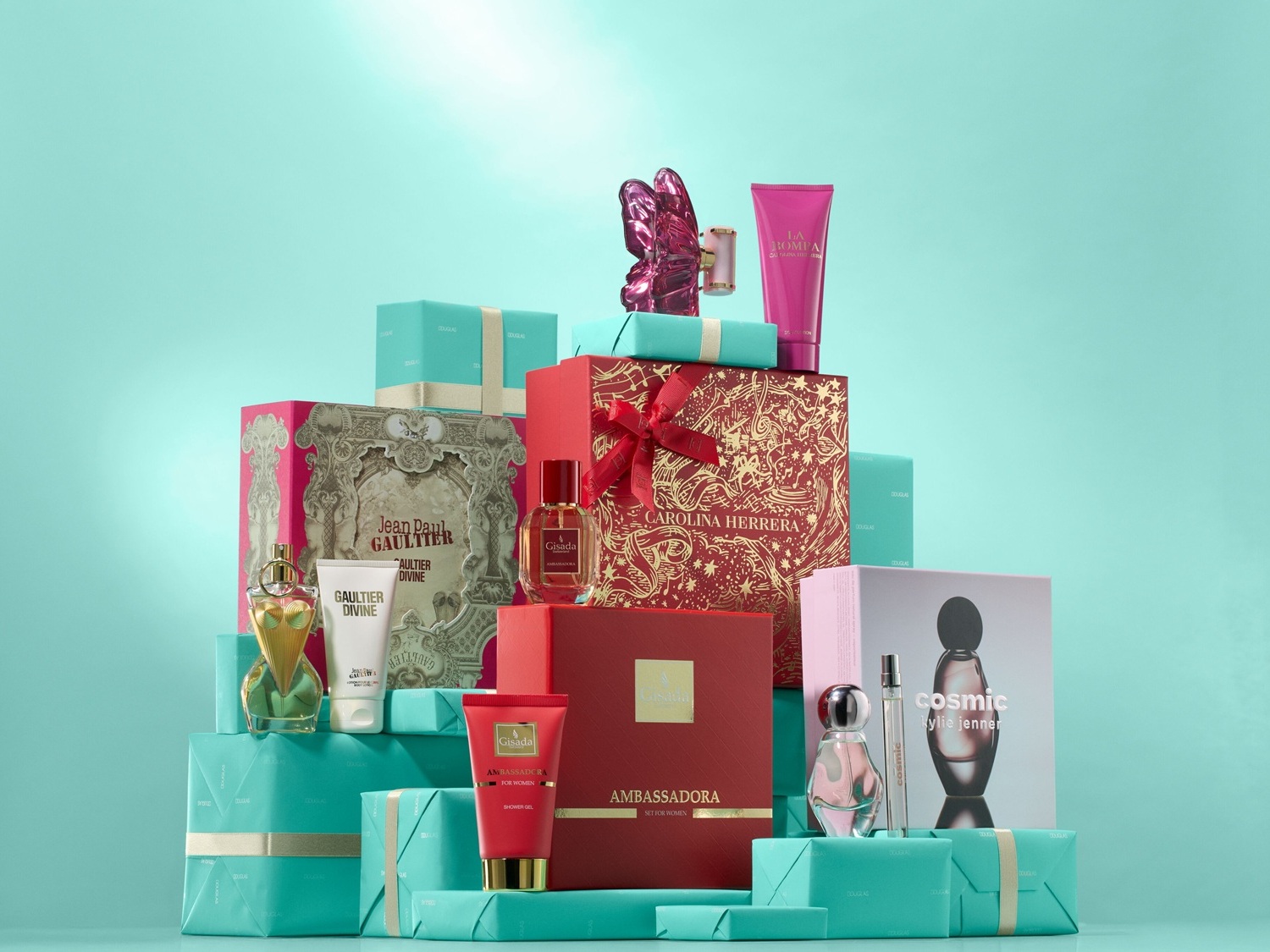 Eine gestapelte Sammlung von Geschenksets, darunter Jean Paul Gaultier, Carolina Herrera und Gisada, verpackt in roten und türkisfarbenen Schachteln.