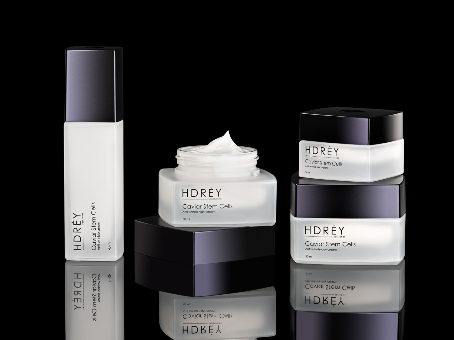 Kolekcja kosmetyków Hdrèy Caviar Stem Cells w białych opakowaniach z czarnymi akcentami, obejmująca serum, krem na noc, krem pod oczy i krem na dzień, zapewniająca kompleksową pielęgnację przeciwzmarszczkową.