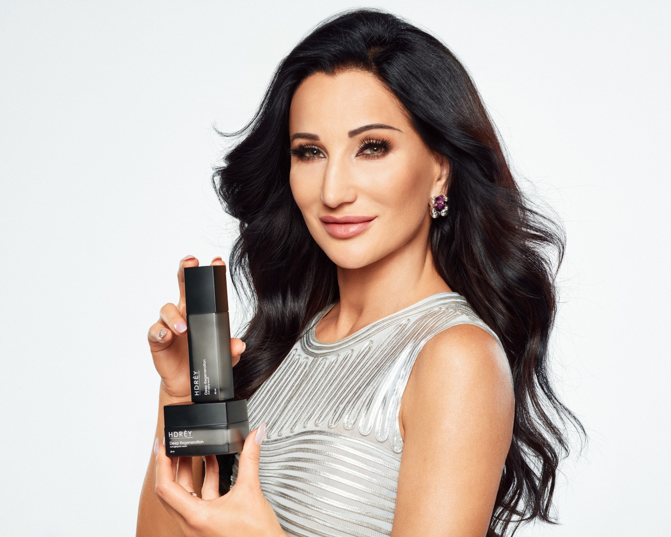 Kobieta z ciemnymi włosami prezentuje zestaw kosmetyków HDRÈY Deep Regeneration w czarnych opakowaniach, obiecujących głęboką regenerację skóry.