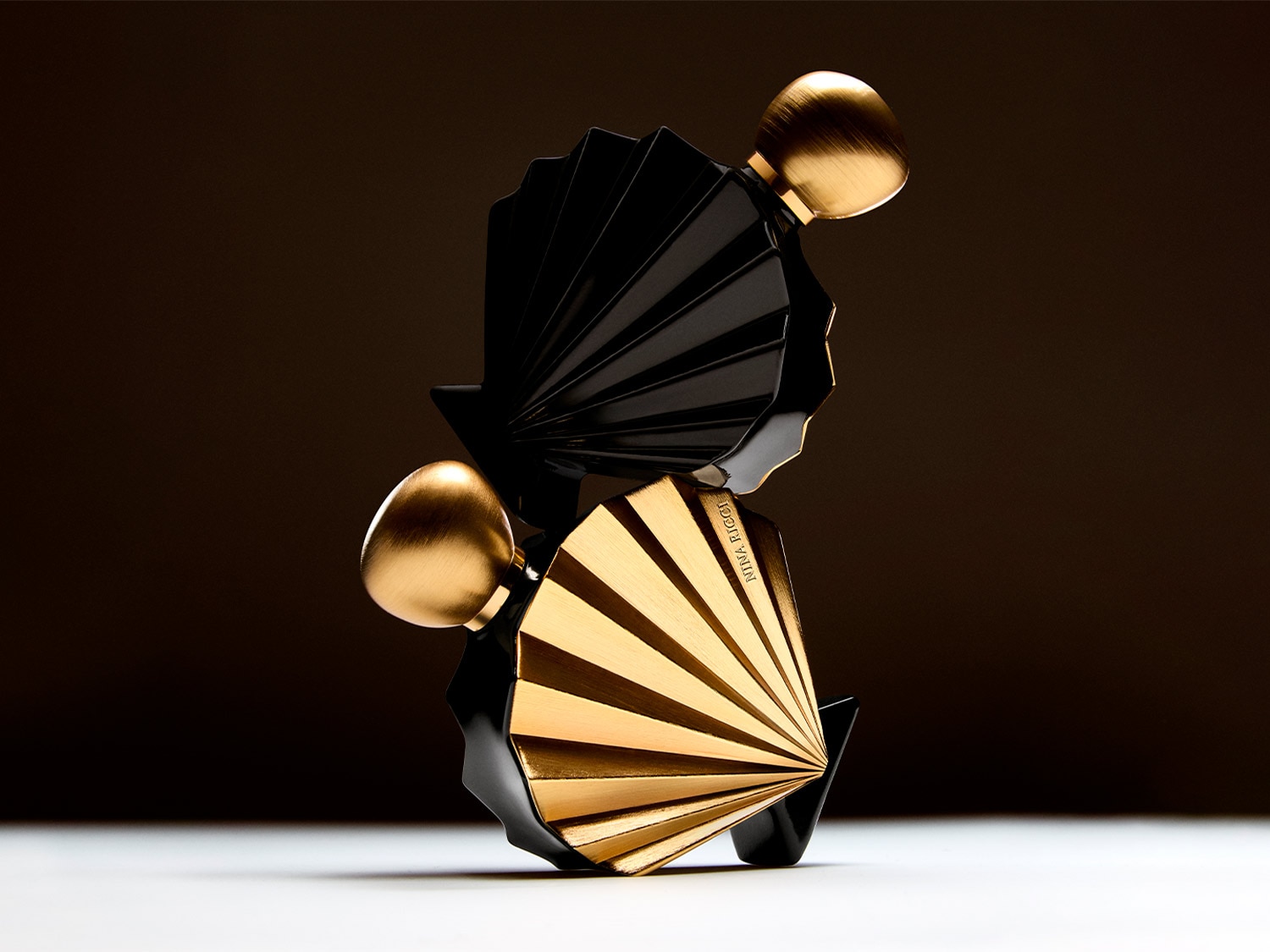 Voici deux flacons de parfum Nina Ricci en éventail, l'un noir et l'autre doré, coiffés de bouchons dorés en forme d'œuf, évoquant luxe et élégance.