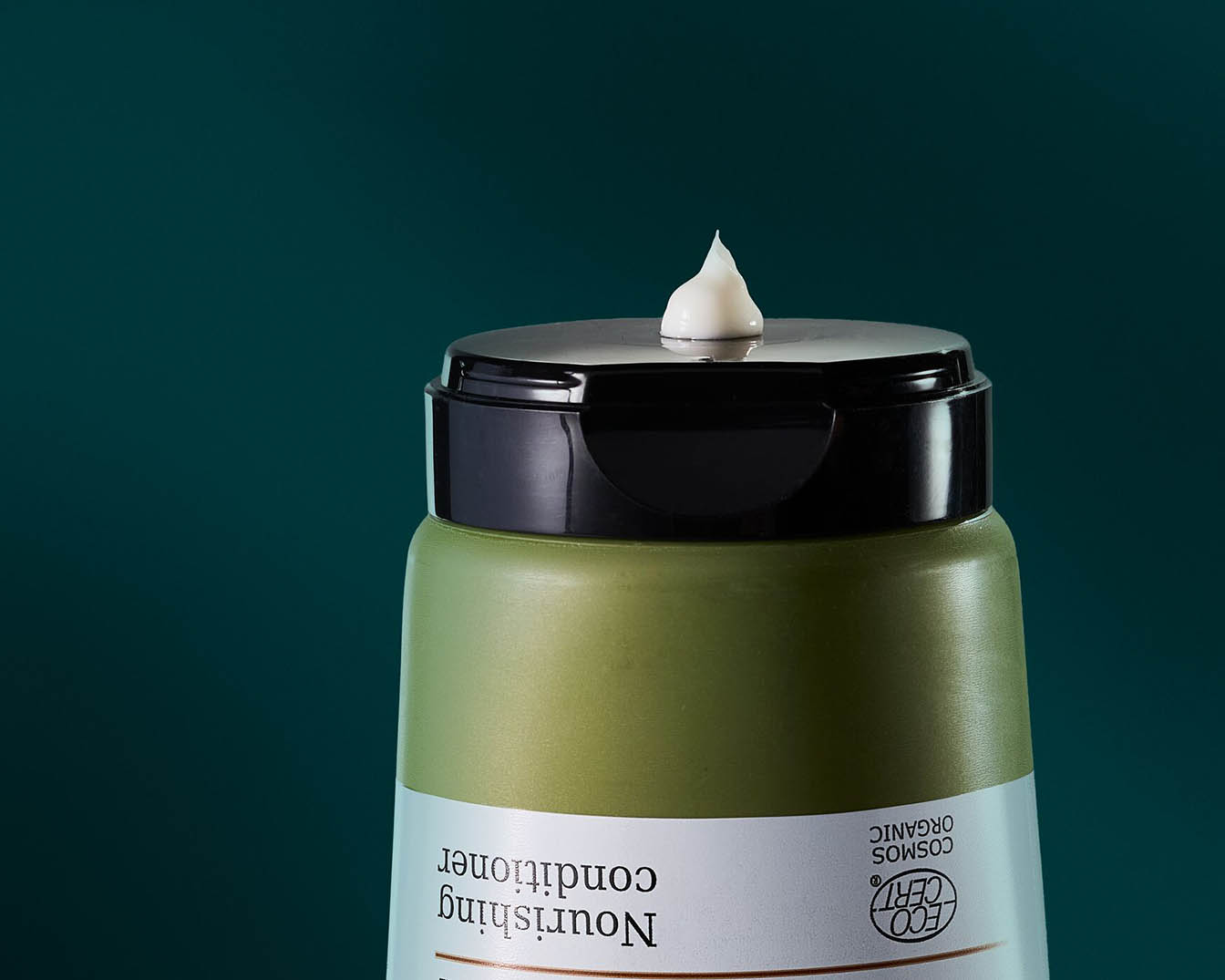 Nahaufnahme einer olivgrünen Flasche mit schwarzem Deckel, auf dem ein Klecks cremefarbener Spülung zu sehen ist.