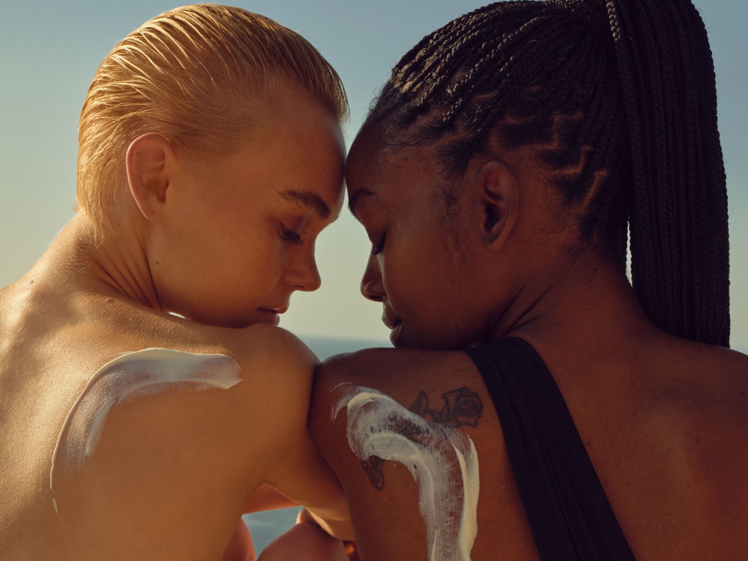 Zwei strahlende Frauen mit geschlossenen Augen lächeln, die eine mit roten, glatten Haaren und die andere mit dunklen, lockigen Haaren.