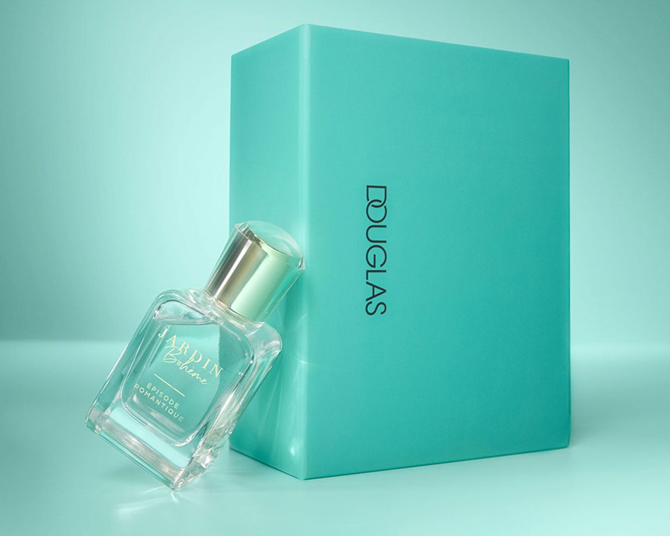 Ein klares Glasflakon von Jardin Bohème Episode Romantique Eau de Parfum lehnt an einer türkisfarbenen Douglas-Box.