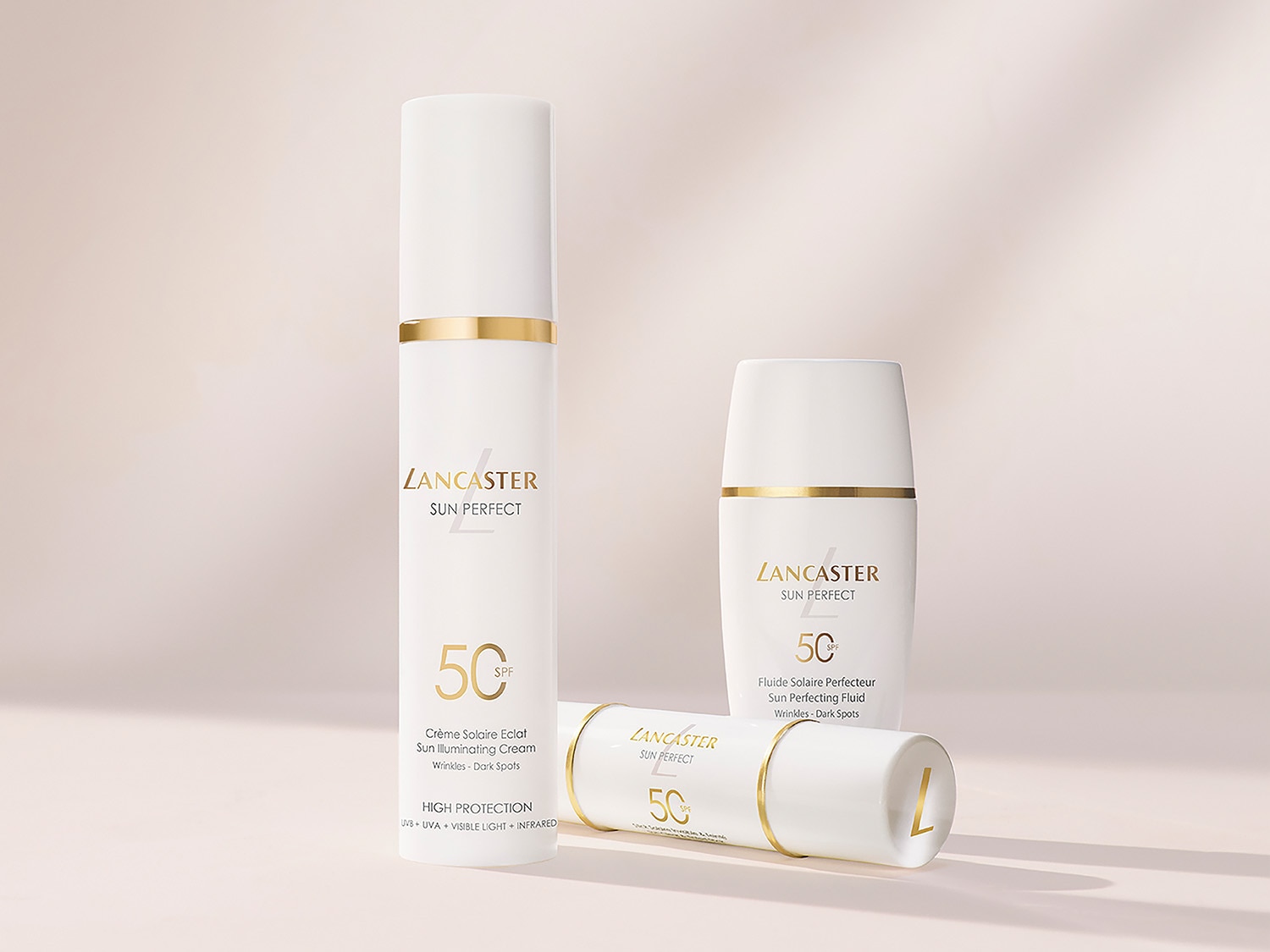 Drei weiße Lancaster Sun Perfect Sonnenschutzprodukte mit goldenen Akzenten, darunter Creme und Fluid mit LSF 50, die vor Falten und dunklen Flecken schützen.