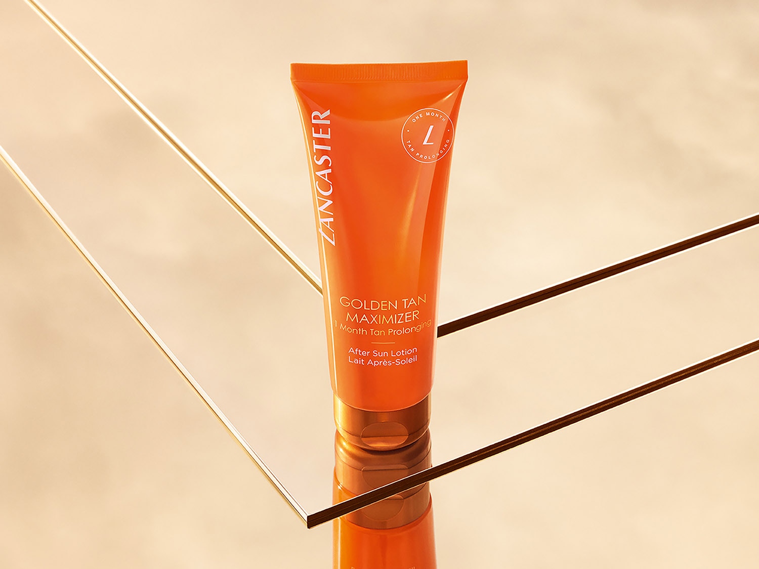 Eine orangefarbene Tube Lancaster Golden Tan Maximizer After Sun Lotion, die einen Monat lang die Bräune verlängert, steht auf einer reflektierenden Oberfläche.
