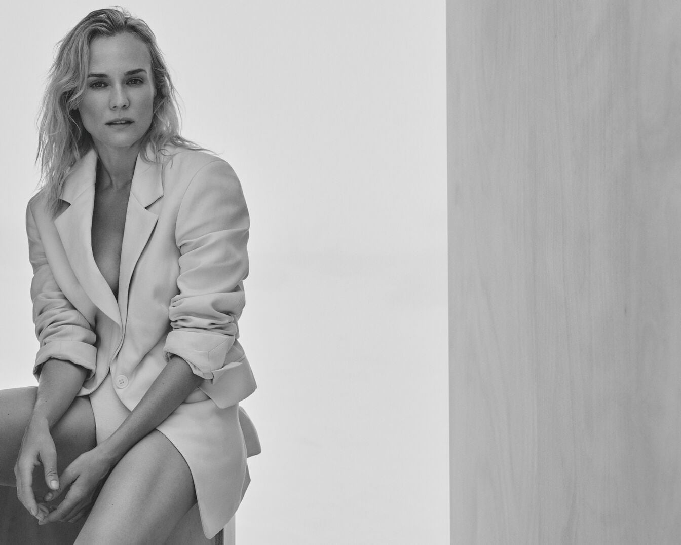 En una foto en blanco y negro, una mujer rubia con una chaqueta clara posa sentada, mirando directamente a la cámara con una expresión serena.