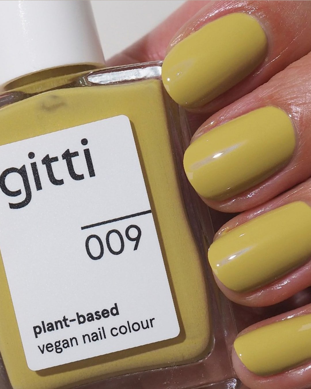 Nahaufnahme einer Flasche Gitti-Nagellack Nr. 009, einer veganen Farbe auf Pflanzenbasis, neben lackierten Nägeln im gleichen gelben Farbton.