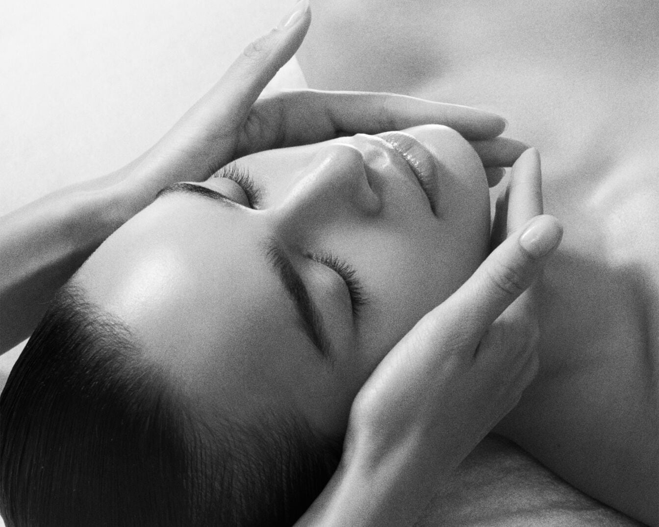 Nahaufnahme einer Frau, die eine entspannende Gesichtsmassage erhält, wobei die Hände sanft ihr Gesicht berühren und ein Gefühl von Ruhe und Wohlbefinden vermitteln.