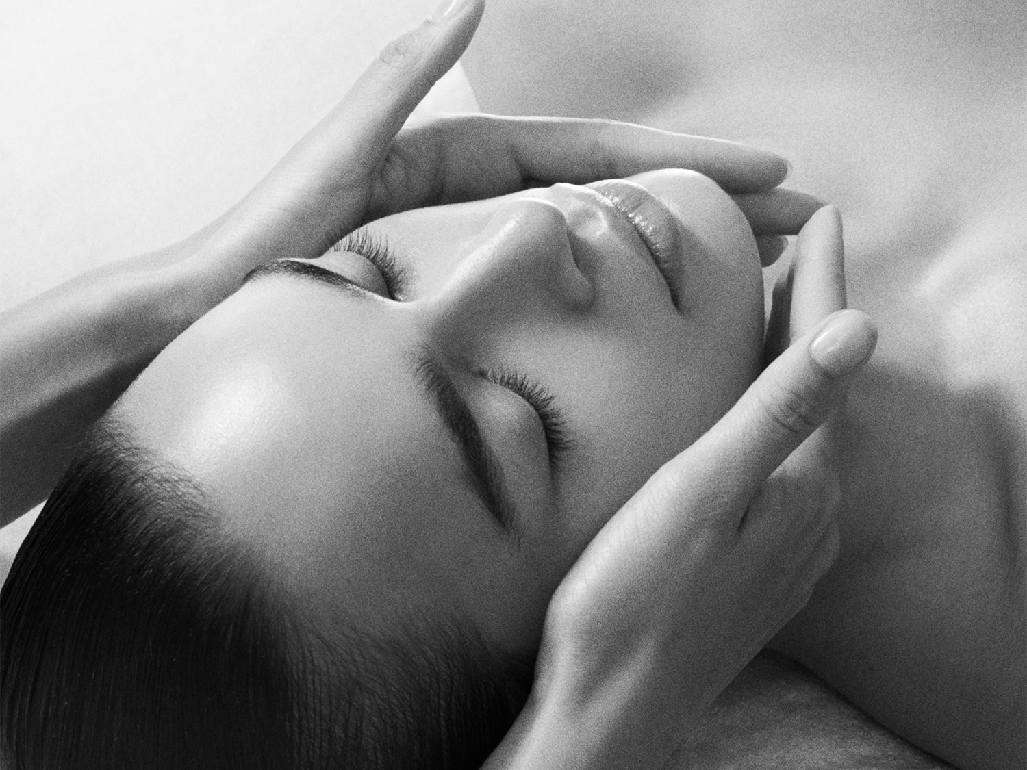 Nahaufnahme einer Frau, die eine entspannende Gesichtsmassage erhält, wobei die Hände sanft ihr Gesicht berühren.