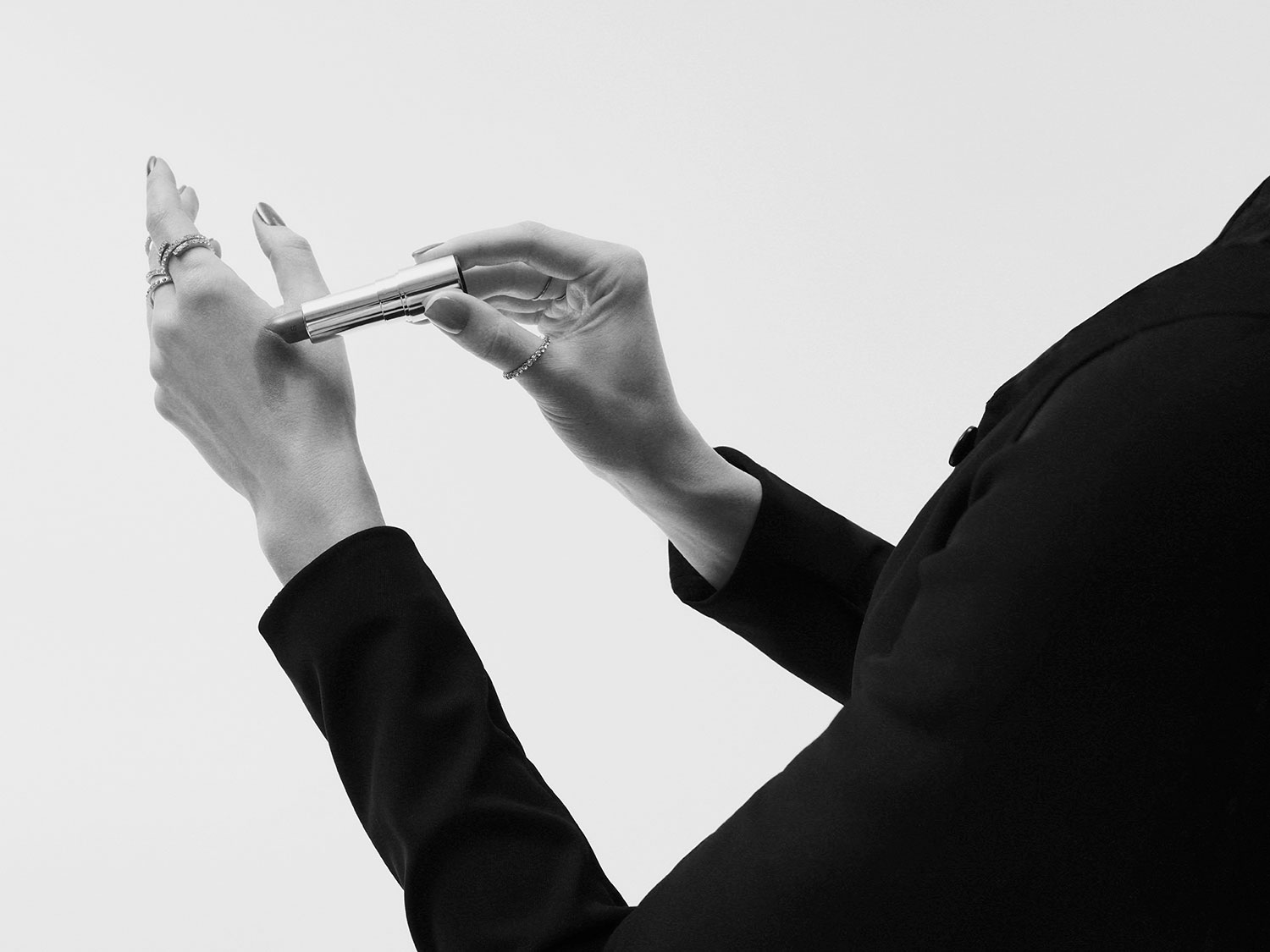 Eine Person im schwarzen Blazer testet einen silbernen Lippenstift auf dem Handrücken, um die Farbe zu prüfen.