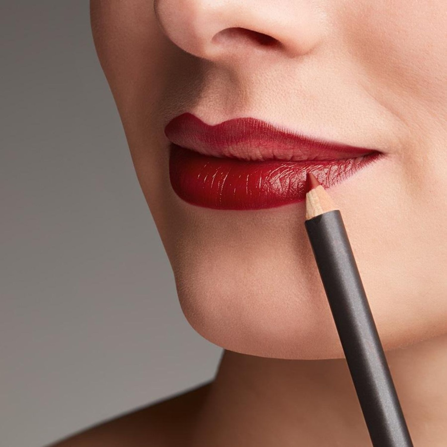 Gros plan sur une femme appliquant un crayon à lèvres rouge foncé pour définir et rehausser ses lèvres.