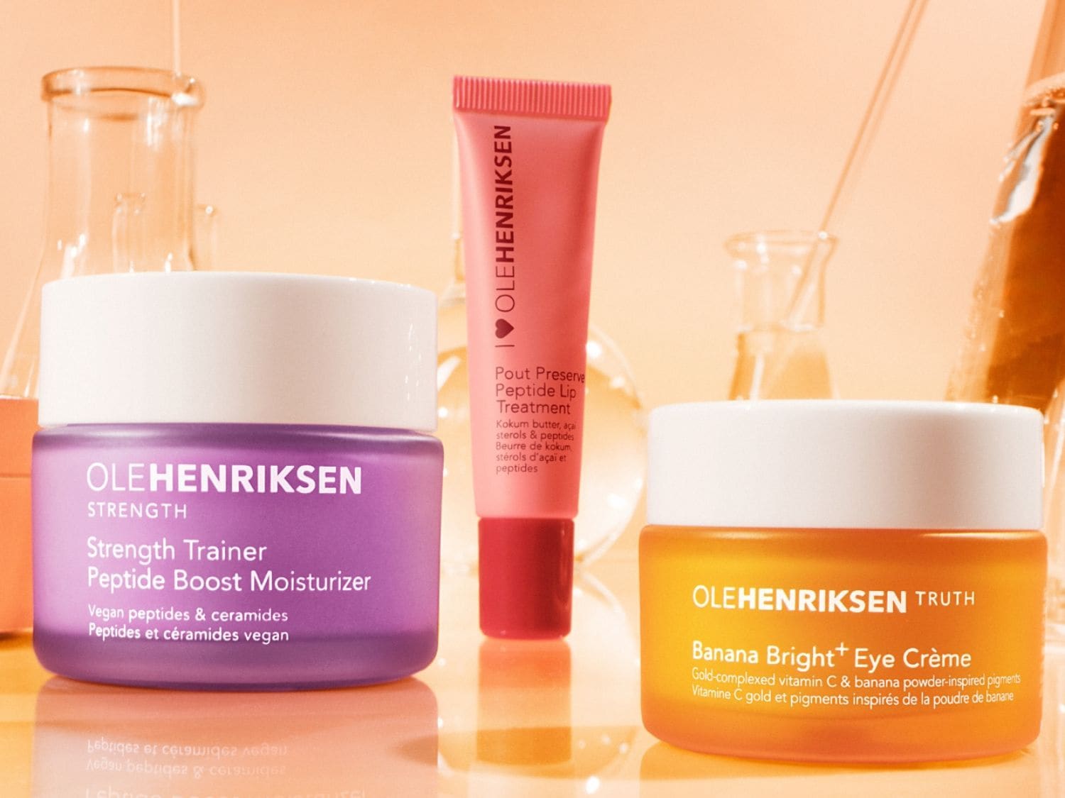 Découvrez le trio de soins Olehenriksen : le pot violet Strength Trainer Peptide Boost Moisturizer, le tube rose Pout Preserve Peptide Lip Treatment et le pot orange Banana Bright+ Eye Crème pour une peau éclatante.