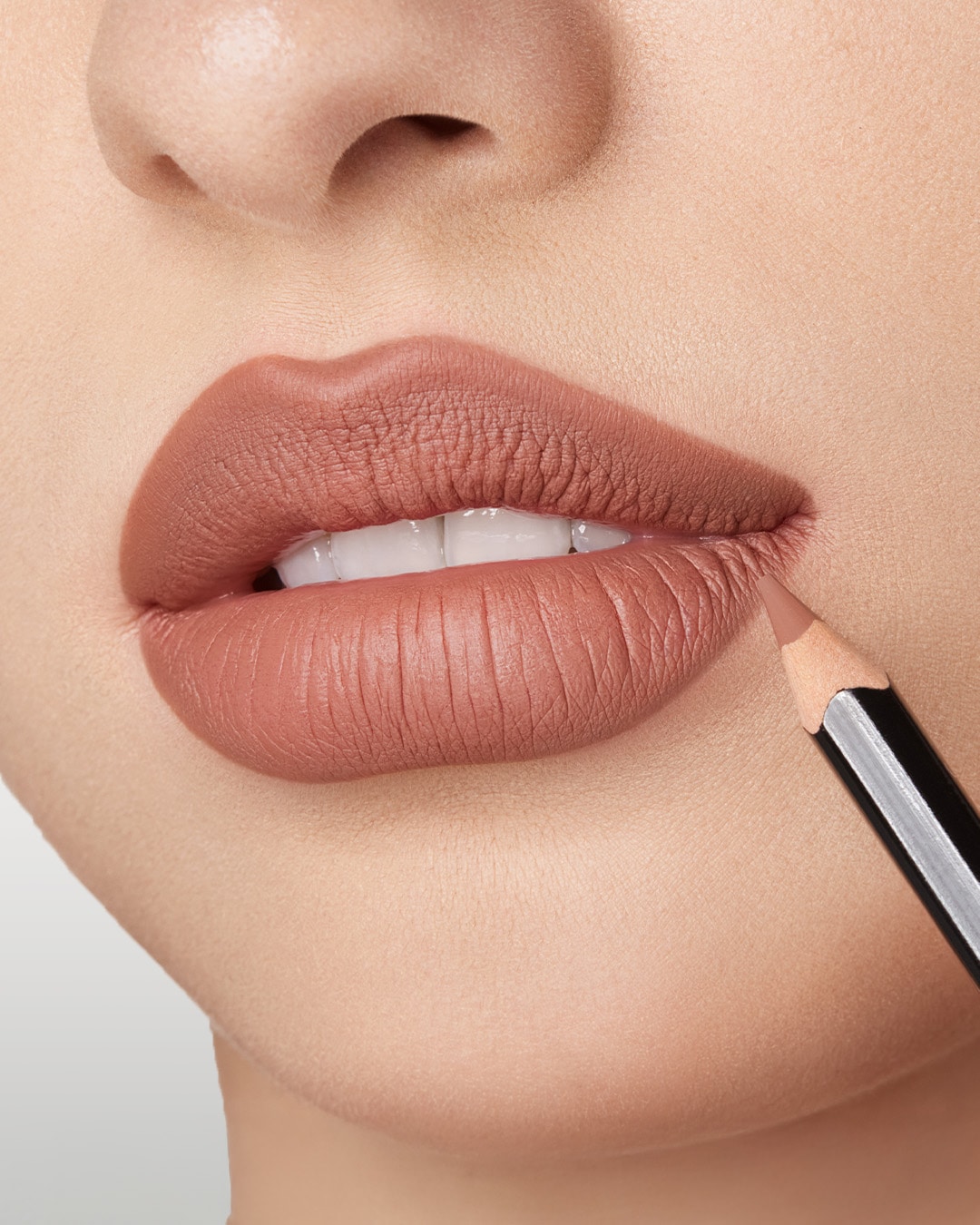 Nahaufnahme einer Person, die einen Lippenstift mit einem Lipliner in einem sanften, matten Rosaton aufträgt.