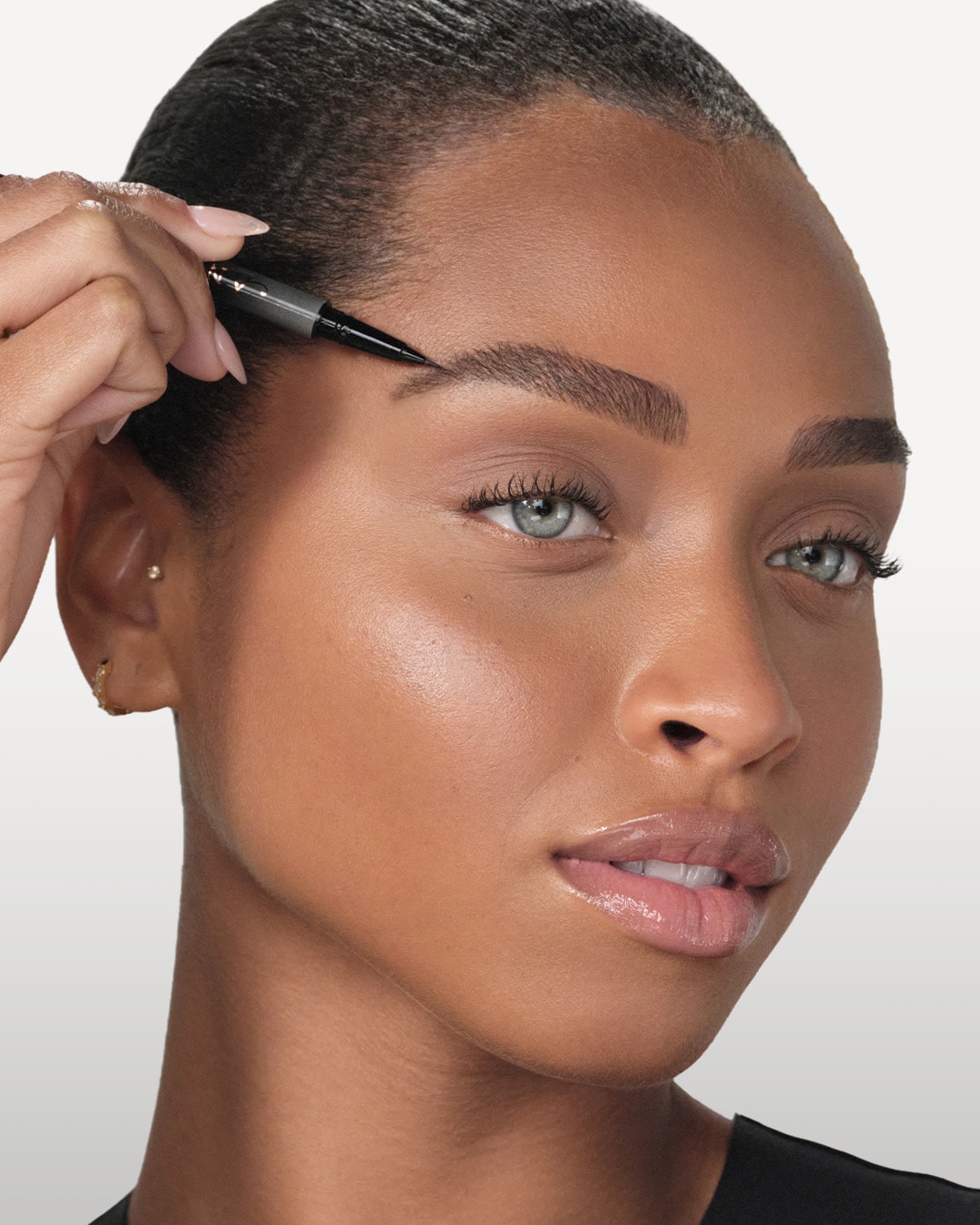 Nahaufnahme einer Frau mit hellblauen Augen, die mit einem Augenbrauenstift ihre Augenbrauen nachzeichnet.