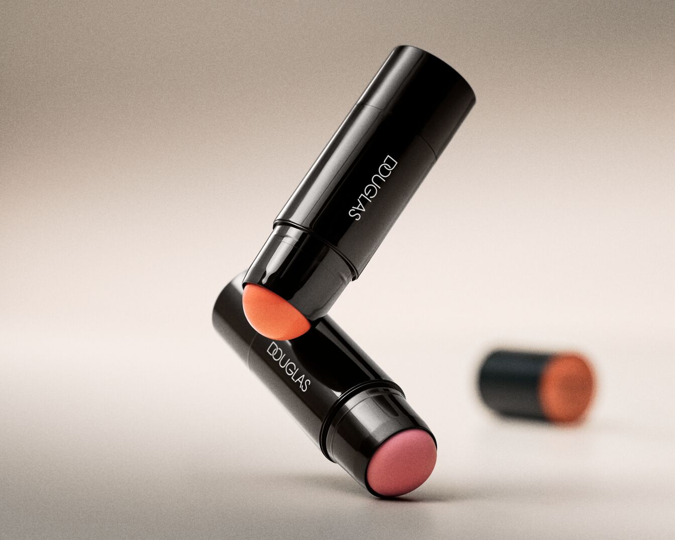 Nahaufnahme von zwei Douglas Make-up-Stiften mit schwarzer Verpackung und einem orangefarbenen und einem rosa Applikator.