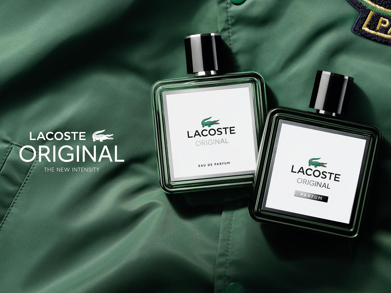 Dwa flakony perfum Lacoste Original: jeden Eau de Parfum, drugi Parfum, oba z logo zielonego krokodyla na białej etykiecie i czarną nakrętką, na tle zielonej kurtki.