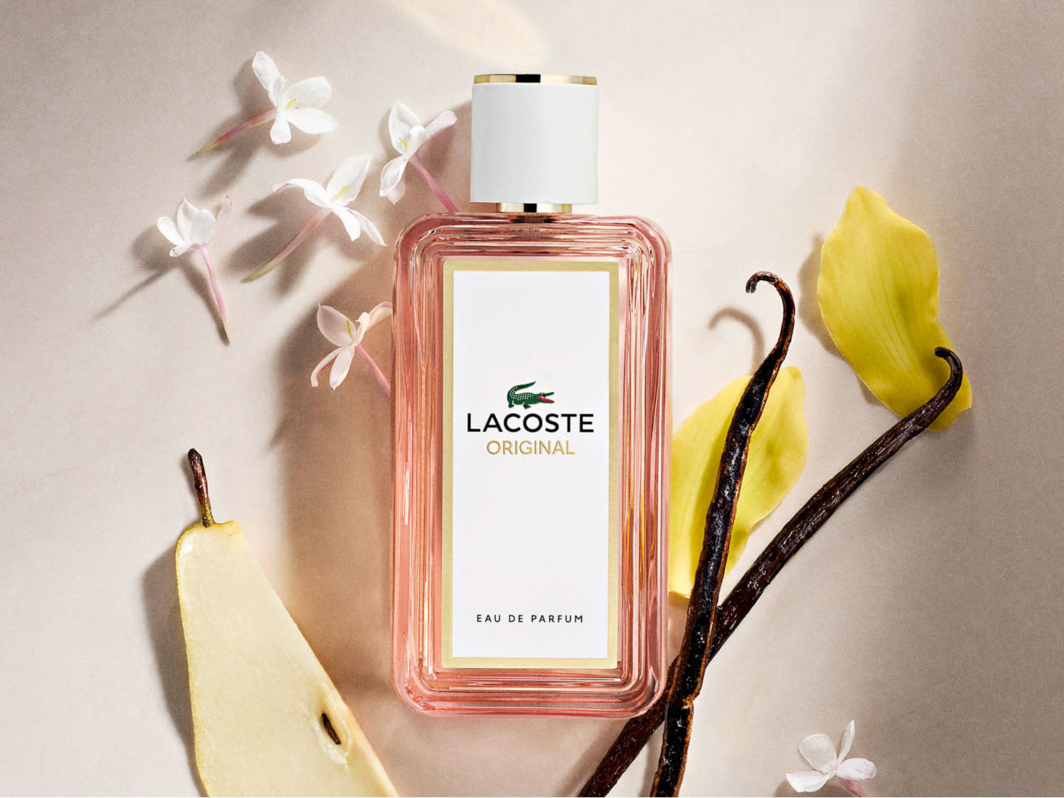 Flakon wody perfumowanej Lacoste Original z białym korkiem i różową zawartością, otoczony kwiatami jaśminu, wanilią i plasterkiem gruszki, tworząc elegancką kompozycję.