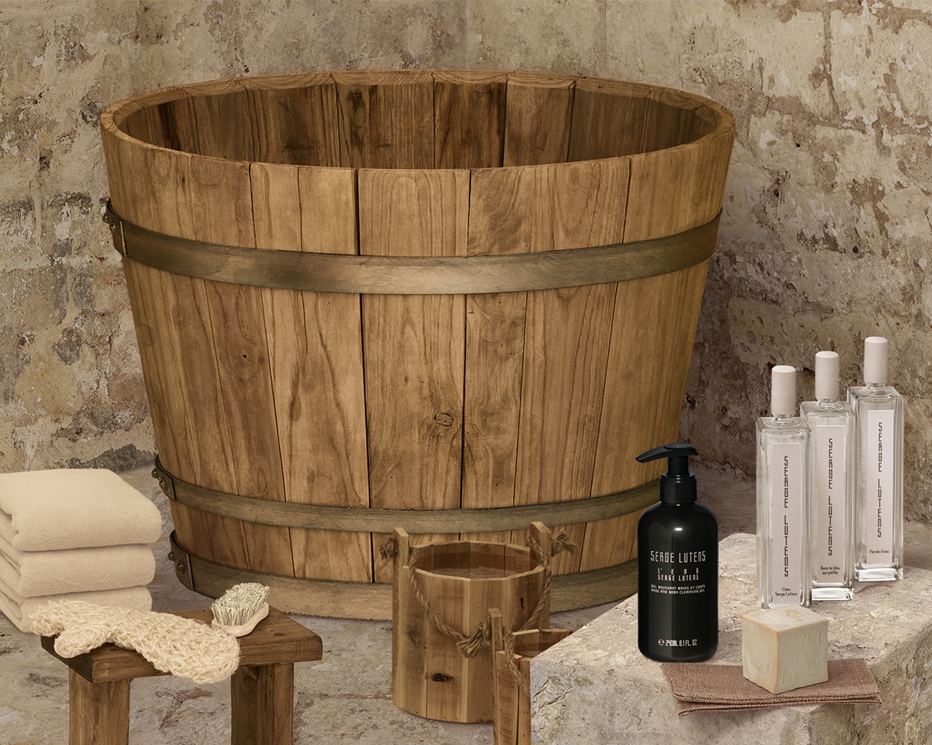 Un cadre serein présente un grand seau en bois, des serviettes moelleuses, et une sélection de produits Serge Lutens, invitant à un rituel de bain luxueux et relaxant.