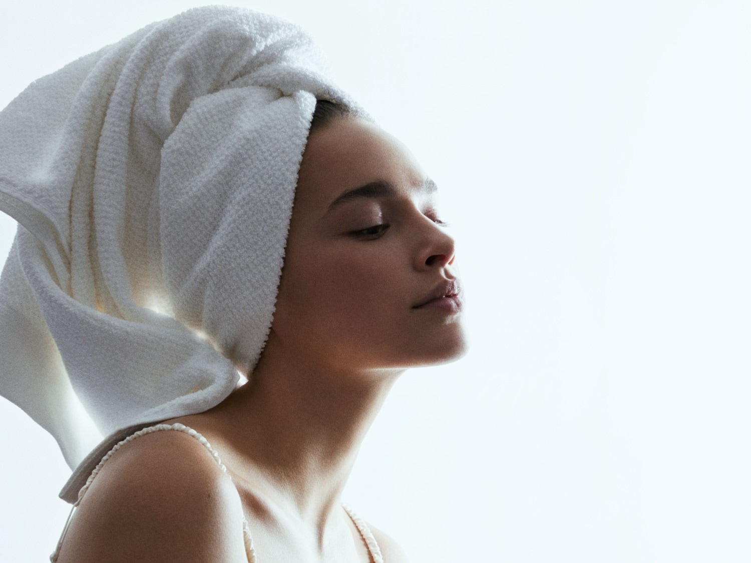 Een vrouw met een witte handdoek om haar hoofd, haar ogen gesloten en haar gezicht naar de zon gericht.