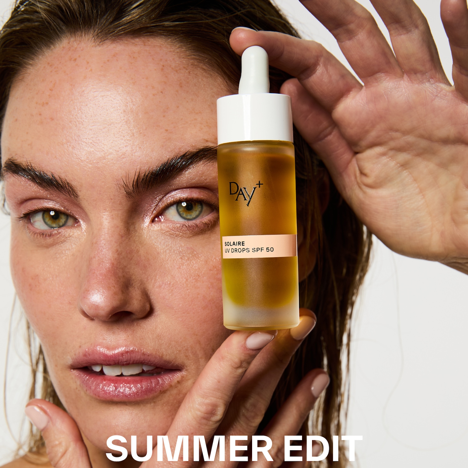 Une femme tient un flacon d'huile solaire Day+ Solaire UV Drops SPF 50, parfait pour l'édition d'été.