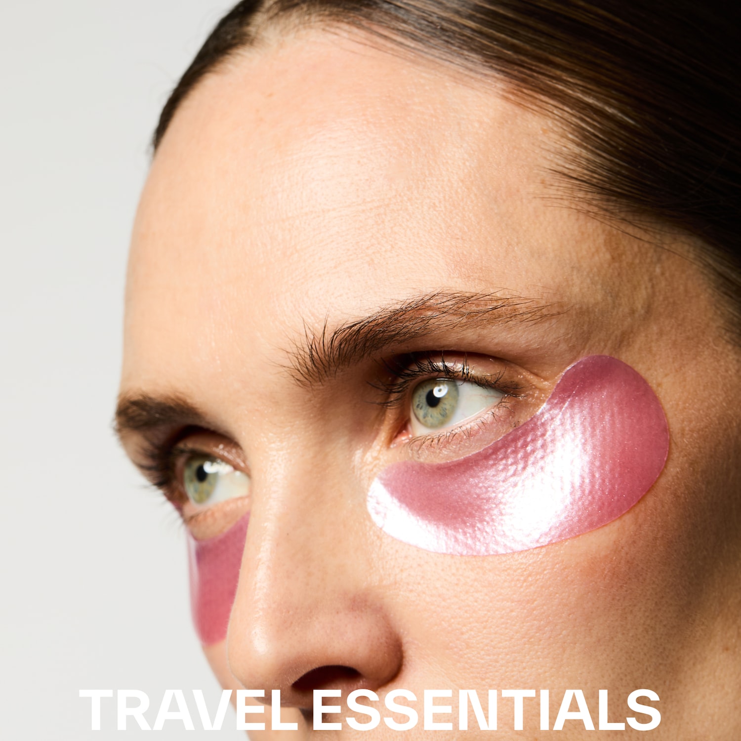 Gros plan sur le visage d'une femme portant des patchs roses scintillants sous les yeux, avec le texte "TRAVEL ESSENTIALS" en bas.