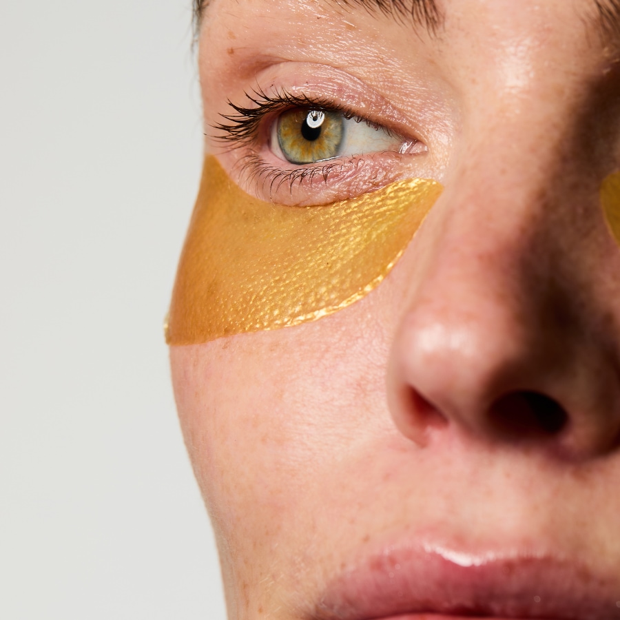 Gros plan sur le visage d'une femme portant des patchs dorés sous les yeux, conçus pour hydrater et illuminer le contour des yeux.