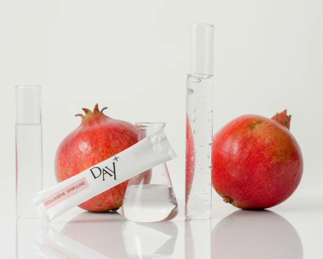 Découvrez Day+, un complément de collagène spiruline présenté dans un emballage blanc, entouré de grenades fraîches et de verrerie de laboratoire.