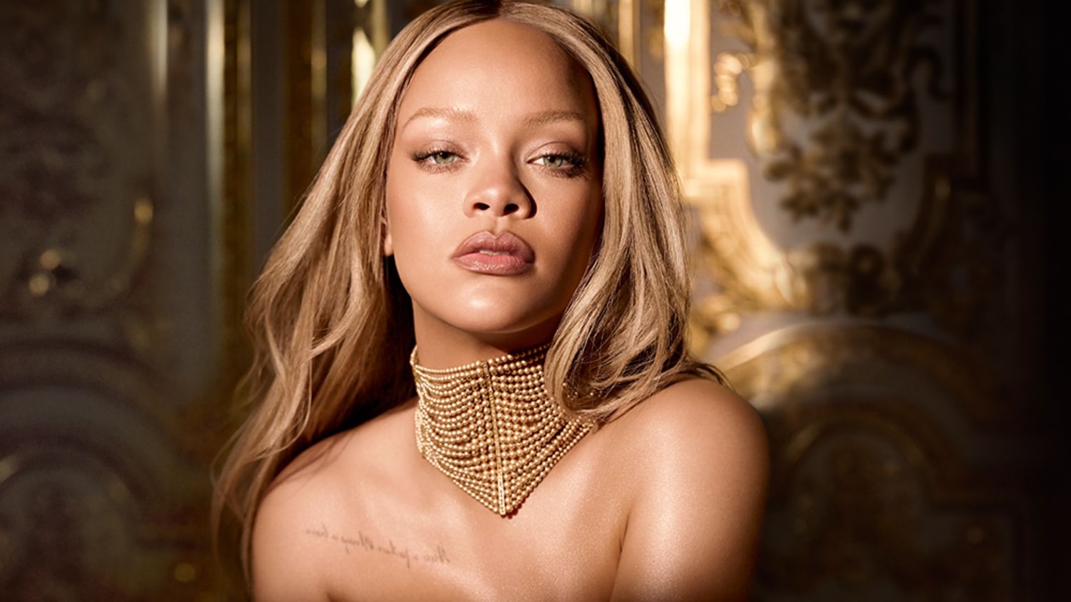 Rihanna szőke hajjal és arany nyaklánccal, természetes sminkben pózol.