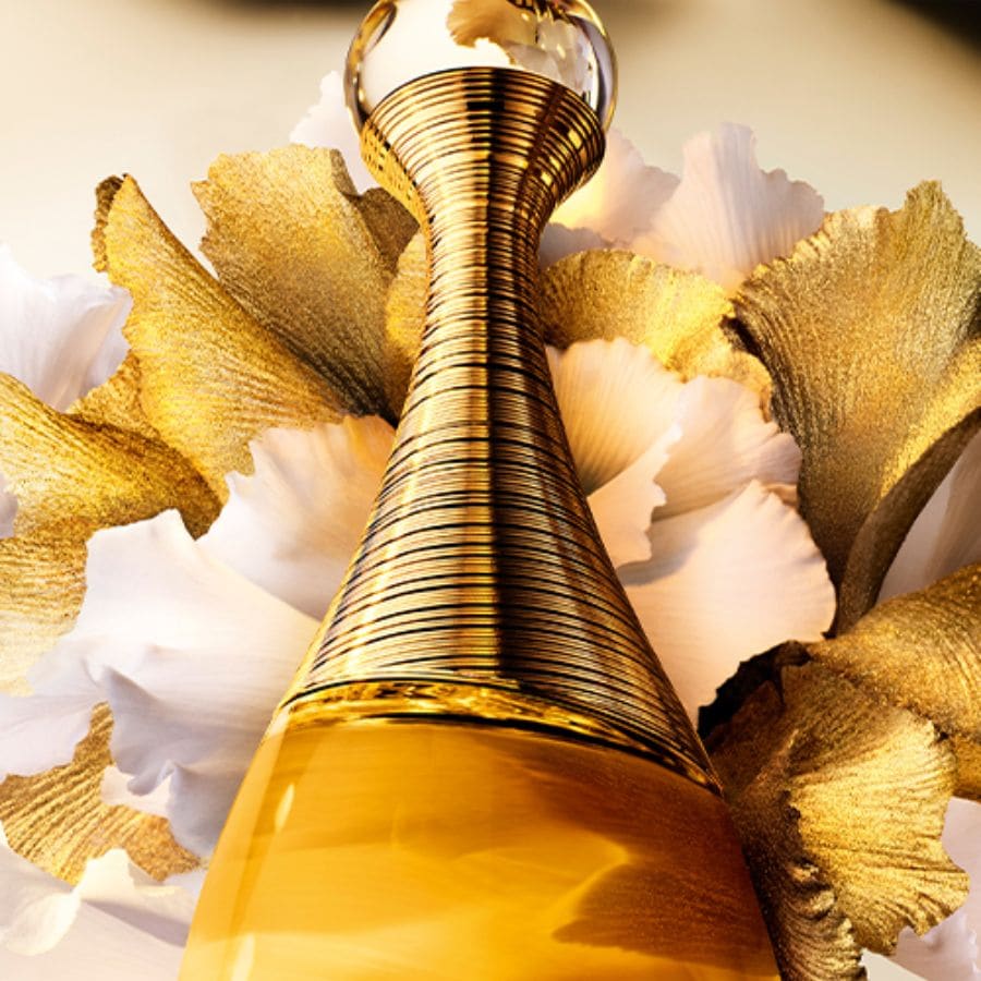 A Dior J'adore parfüm üvege látható, arany színű, virágokkal körülvéve, elegáns és fényűző megjelenést kölcsönözve.