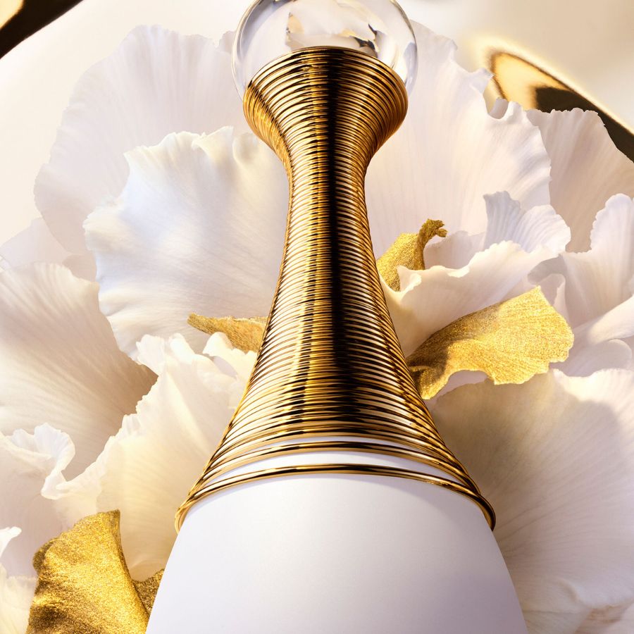 A Dior J'adore ikonikus arany nyaklánca egy fehér virágos háttér előtt, a luxus és az elegancia megtestesítője.